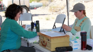 Two people sitting at a table preparing to band birds
