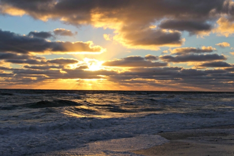 a majestic sunrise glows through the clouds over a beach on the coast of the Atlantic