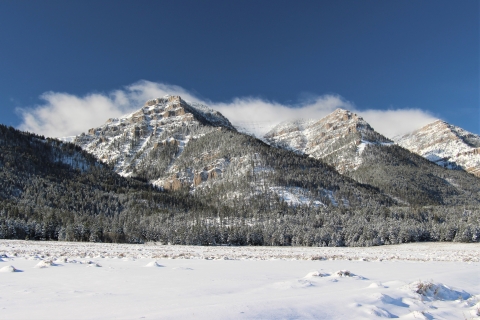 Snow blankets foothills and mountains under blues skies as wispy clouds form atop mountain peaks.