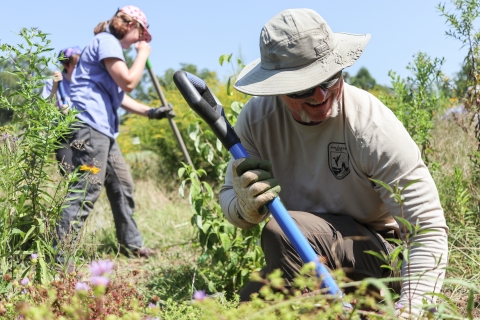 Person kneeling down, working with a shovel, with other workers in the background