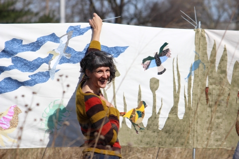 A woman stands next to a fabric artwork hanging outdoors
