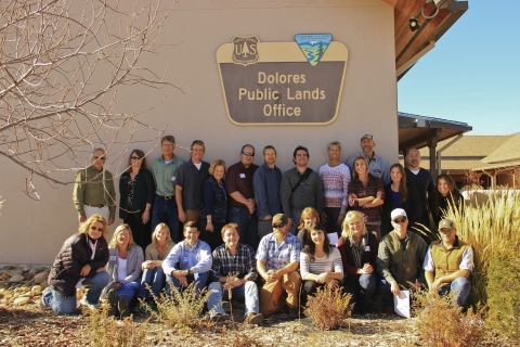 A group of individuals pose in front of a building with a sign that reads "Dolores Public Lands Office"