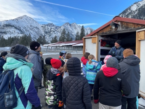A group of students face an instructor with mountains in the background