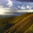 vegetated land sloping towards the Pacific Ocean with rays of sunlight appearing through clouds