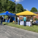 A blue USFWS canopy next to a yellow canopy. People are standing around the tables that are underneath the canopies. 