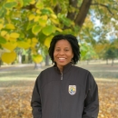 Shanice smiles with hands in pockets. She is wearing a black FWS zip up jacket.