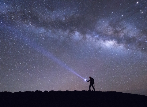 The silhouette of a hiker walking with the night sky illuminating them 