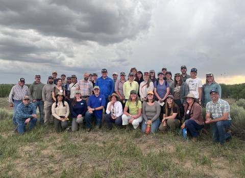 thirty-six people pose for a photo outdoors with a cloudy sky