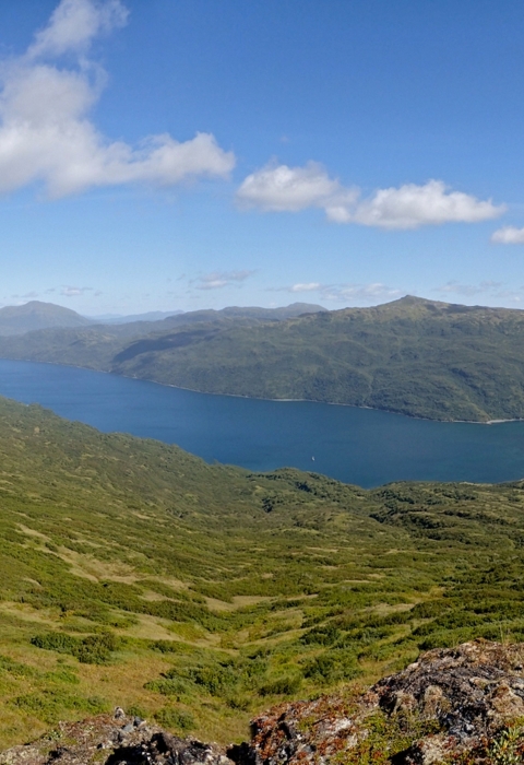 Cerulean blue water stretches between sloped mountains beneath a partly cloudy sky.