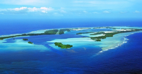 Aerial view of an island atoll surrounded by sandy reef in the deep blue ocean