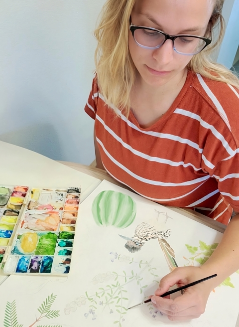Photo of a woman painting a desert scene using watercolors