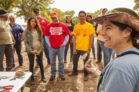 A smiling young woman in foreground holds a bird while a small group of people watch.