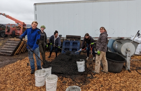 5 youth workers measuring out a brown, soil-like material onto a grate
