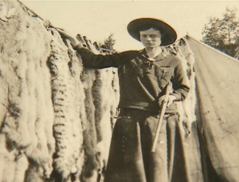 a person standing in front of wolf pelts with gun in hand