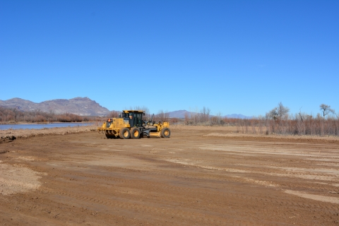 A construction vehicle on a sandy area near a body of water