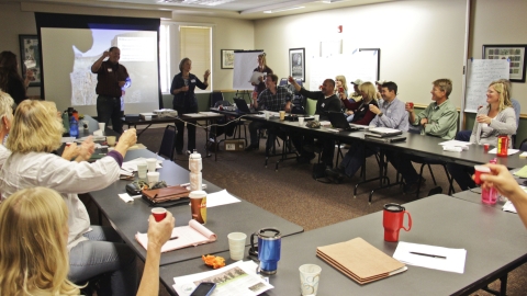 Individuals sit around tables in a conference room and make a toast with small red cups