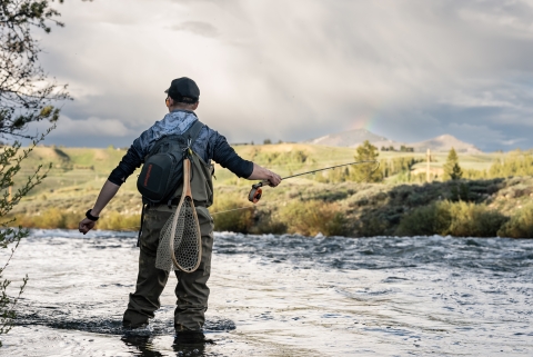 Flyfishing angler in waders casts into a river 