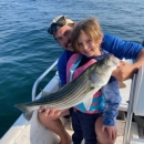 A man and child holding a fish while standing on a boat.