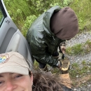 Biologist smiling while lifting a boot up to have friend clean dirt out of tread. 