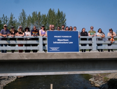 a group of people standing on a bridge over water holding a blue sign