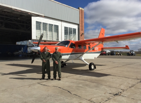 2 people stand in front of an airplane