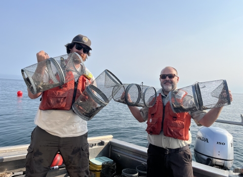 Two biologists holding up four metal minnow traps in a boat.