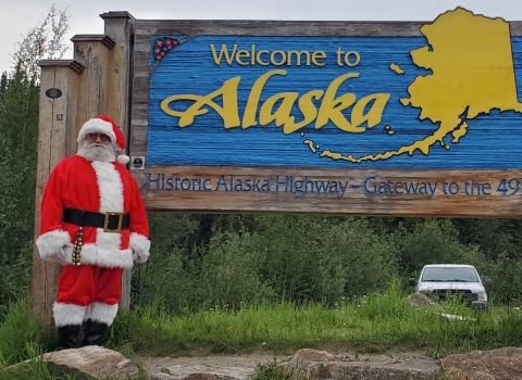 Watercraft inspector, Steve Wogtech, posed in Santa suit in front of Welcome to Alaska sign.