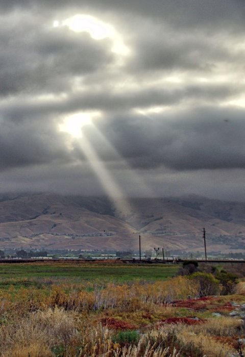 Sun rays shining through dark clouds over a green-and-brown landscape