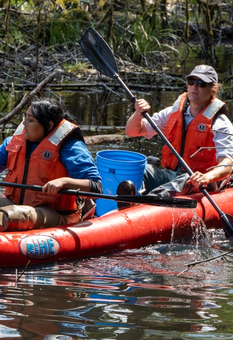 Service intern, Suzena Arias, and employee rafting through wetland to check minnow traps