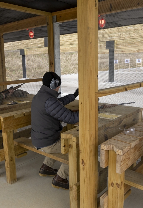 People sitting on wooden benches holding firearms and shooting at a range