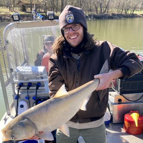 Image of Tyler Gross holding an invasive carp in a boat.