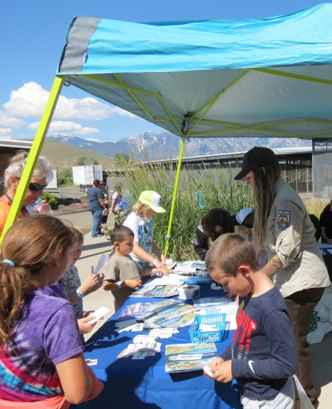 Kids and adults looking over a fun booklet under a canopy shelter during an outdoor event.