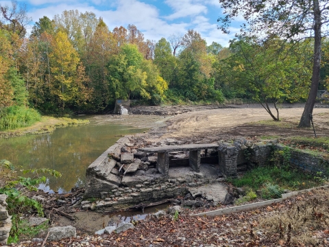 Looking at the site where the old Markle dam was after removal. There is low flow and multicolored trees in the background and rubble of the old mill in the foreground.