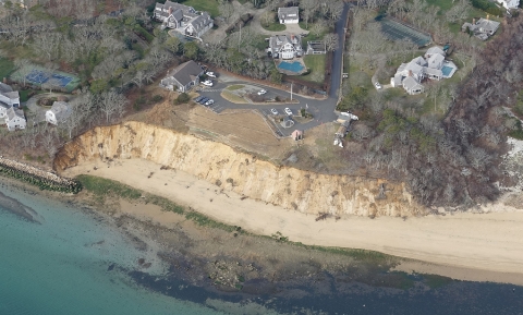an aerial view of an eroding coastal bluff on a national wildlife refuge property. Buildings, a parking lot and trees can be seen surrounding the property