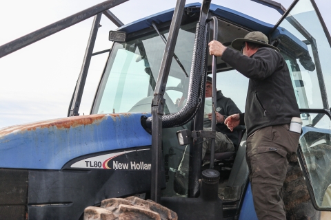 Person standing outside a tractor talking with someone inside the tractor
