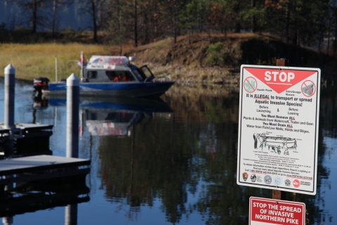 A sign in front of a body of water warning visitors to stop the spread of invasive species