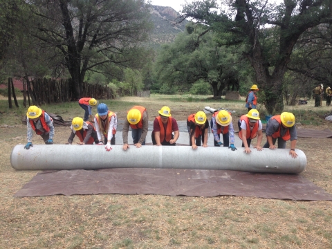 A crew of individuals unroll a large sheet on the ground