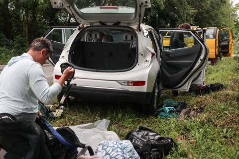 Biologists standing near vehicles, one pulling snorkel gear from a bag the other donning a wetsuit