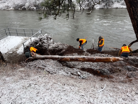 4 people in orange safey vests clean up woody debris from flooding in light snow conditions at leavenwort national fish hatchery