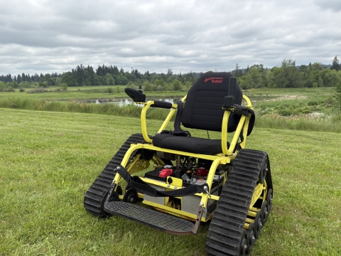 Track chair for adaptive trail use shown on a mowed grass lawn with a wetland in the background.