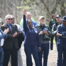 A smiling woman raises her arm high while a group of people standing around her smile at her and applaud.