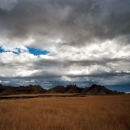 Image of Badlands National Park showing a grassland in front of large geologic formations on an overcast day