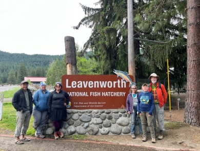 A group of six stands by the Leavenworth National Fish Hatchery entrance sign