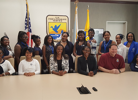 FWS employees and Zeta Phi Beta Sorority sitting and stand with official Service logo and flags in the background. 