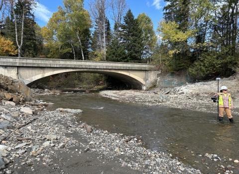 A large concrete bridge spans over a free flowing river, where a dam once impeded water flow.