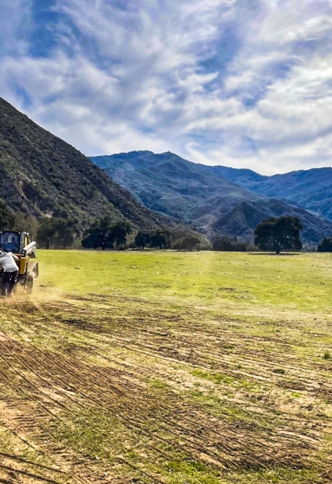 A drill seeder being pushed along a wide open field