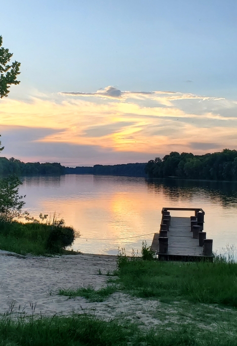 Sunset going down behind clouds over a river with a dock.