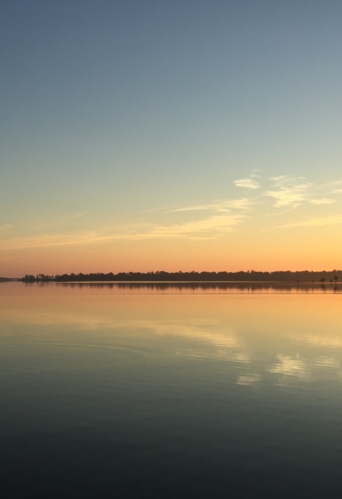A pastel orange sunset reflects in a placid lake bordered with forest