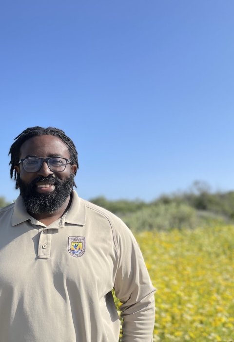 A man wearing a long sleeved polo stands in front of a field with golden flowers