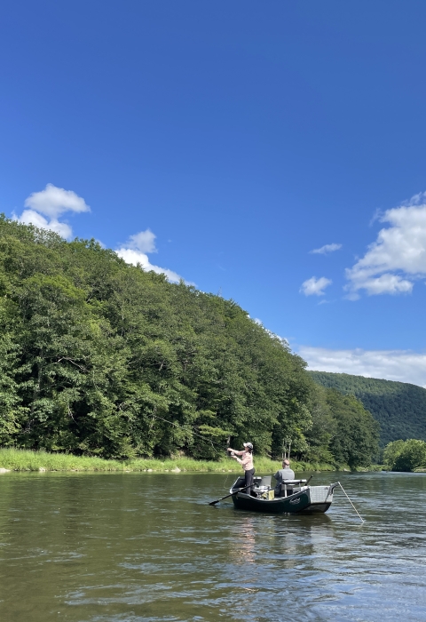 2 people in a boat on a waterbody surrounded by trees with a mountain in the background